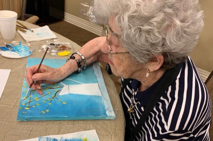 Senior Woman Painting Flowers In Vase At Class